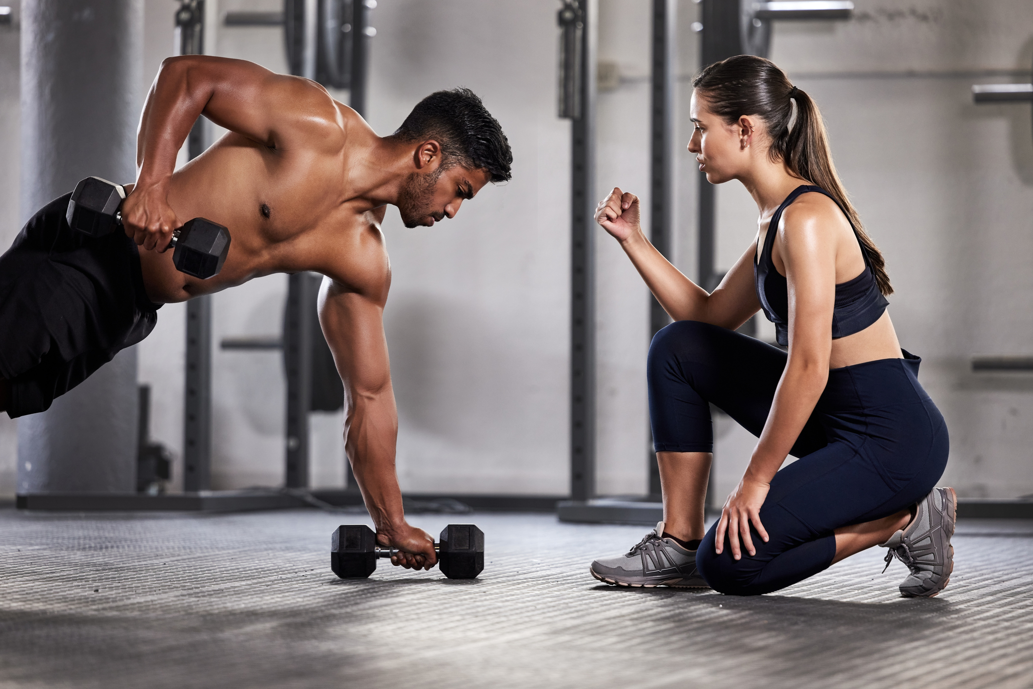 Training, exercise and motivation with a fitness coach or personal trainer and her bodybuilder student during a workout in the gym. Health, sports and wellness with a heathy athlete exercising