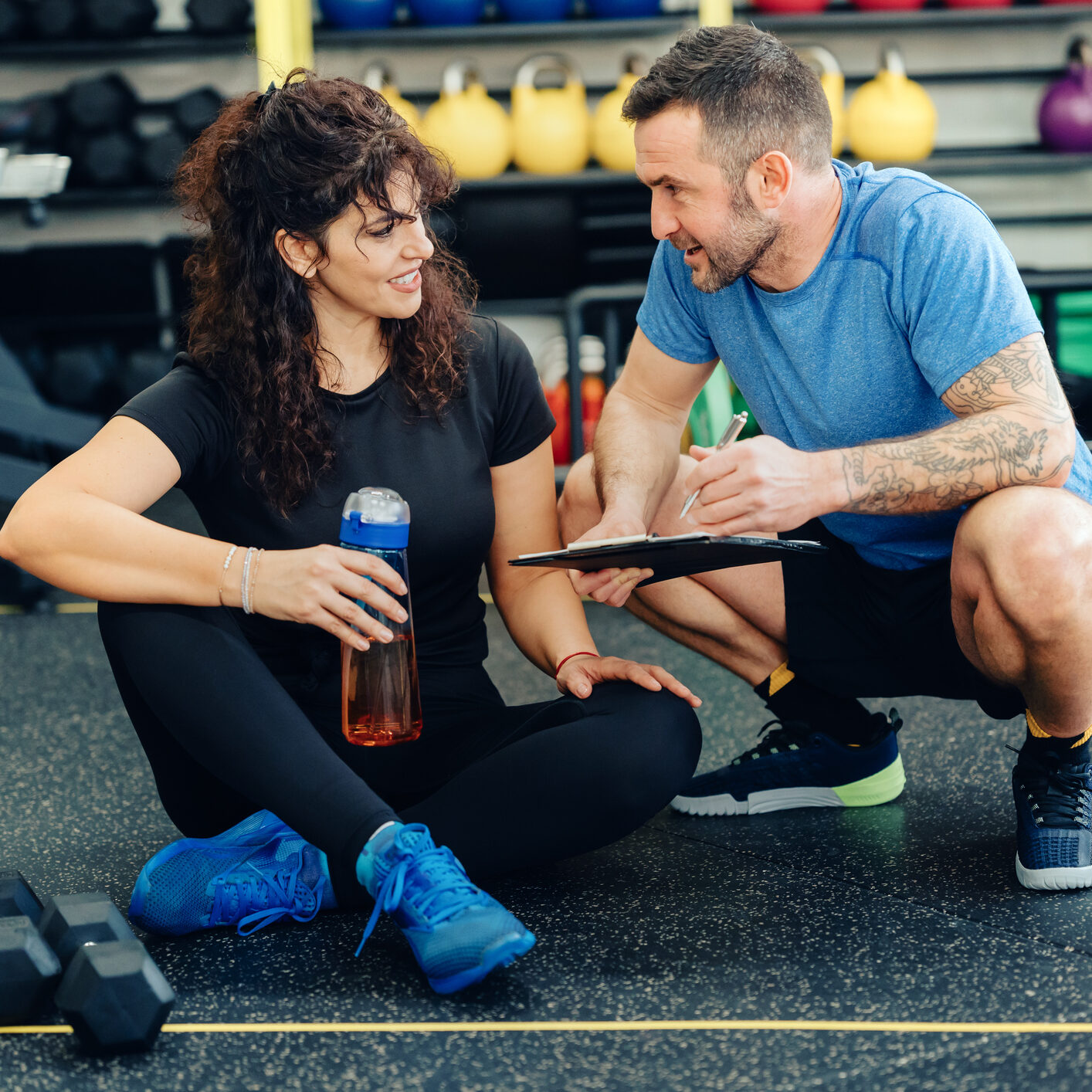Sportswoman and her fitness instructor analyzing workout plans in the gym.